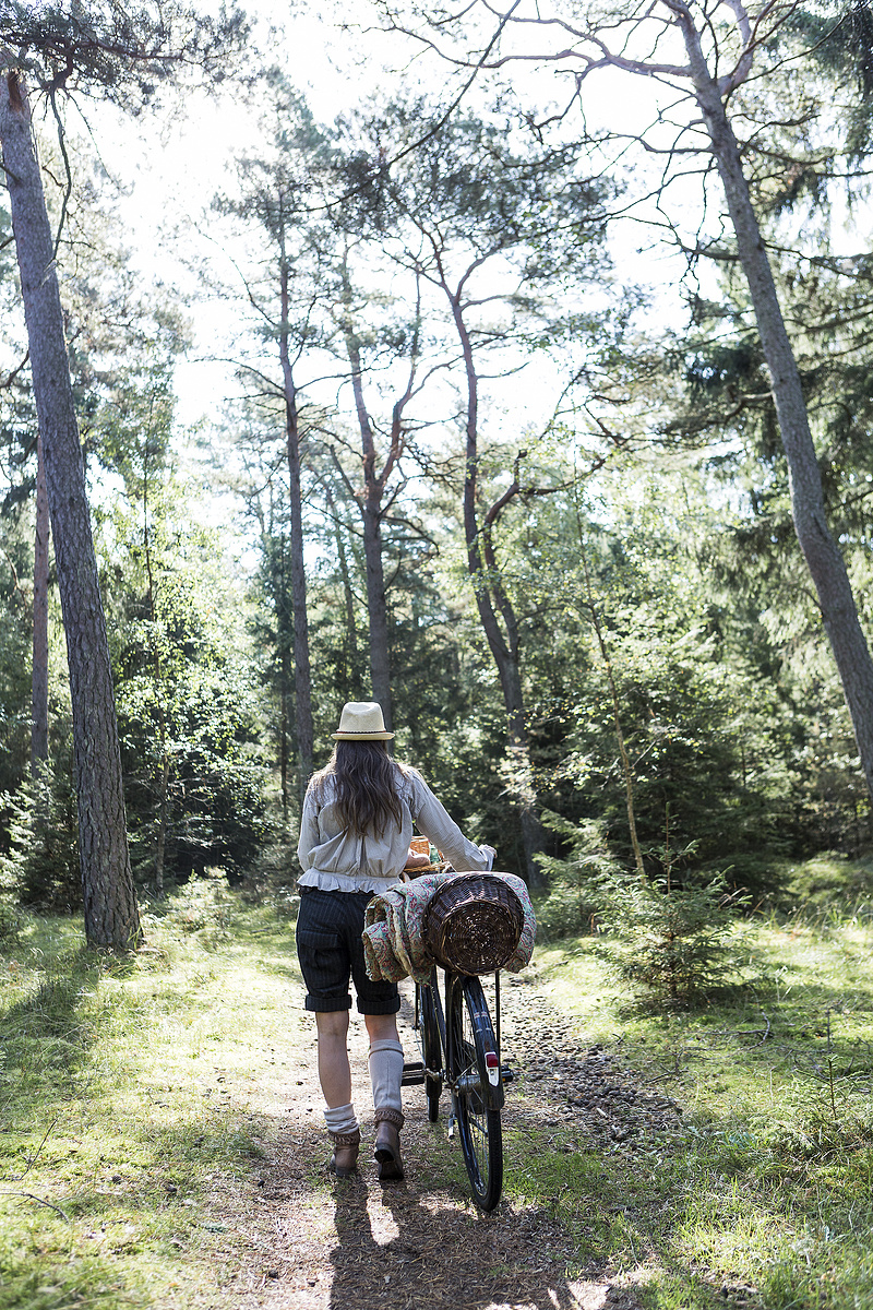 一名成熟女子在森林小路上推着自行车背着觅食篮子图片