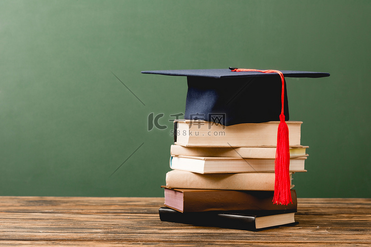 书籍和学术帽在木制表面隔离在绿
