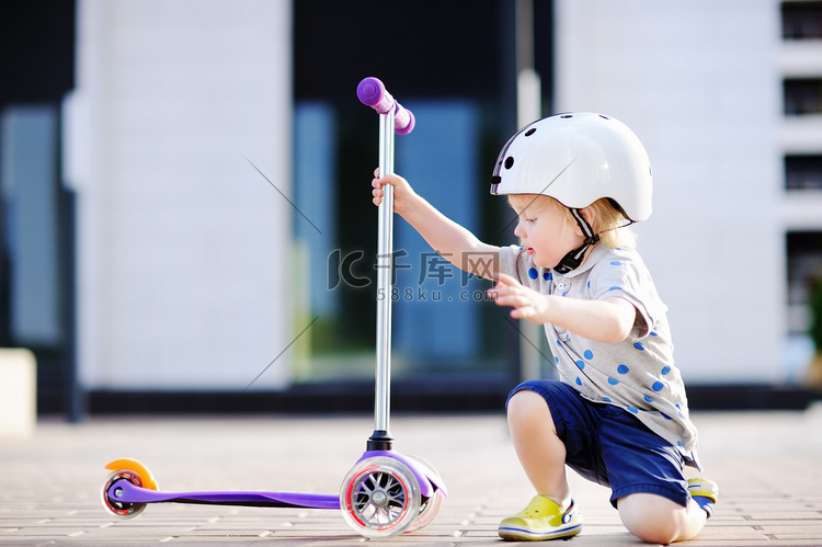 蹒跚学步的小男孩学骑滑板车 