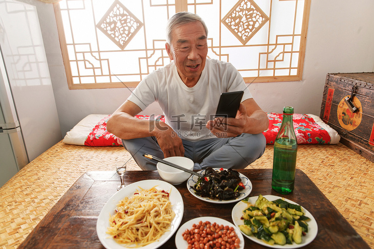 老年人坐在家里吃饭看手机