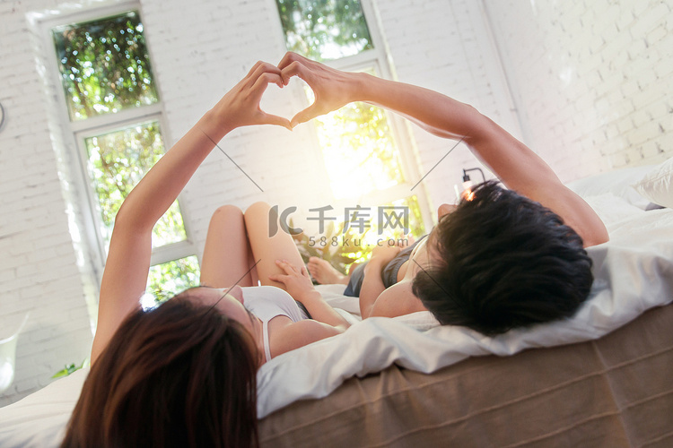 幸福的年轻伴侣躺在床上做心形手