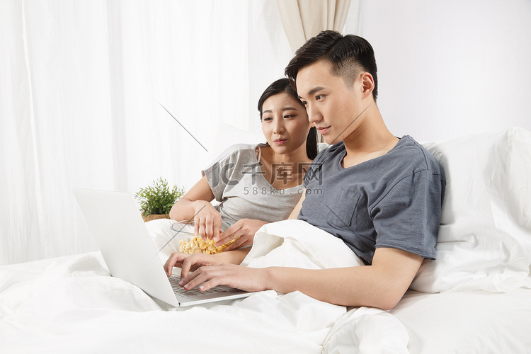 青年情侣坐着床上看电脑