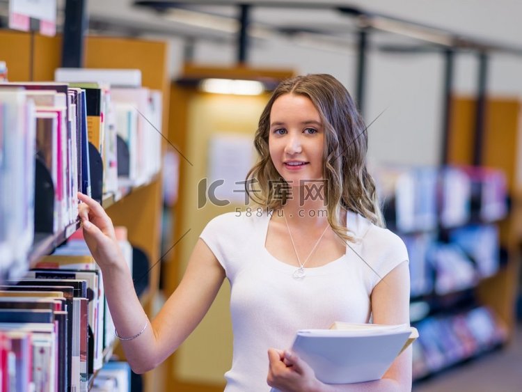 快乐的女学生在图书馆里拿着书。