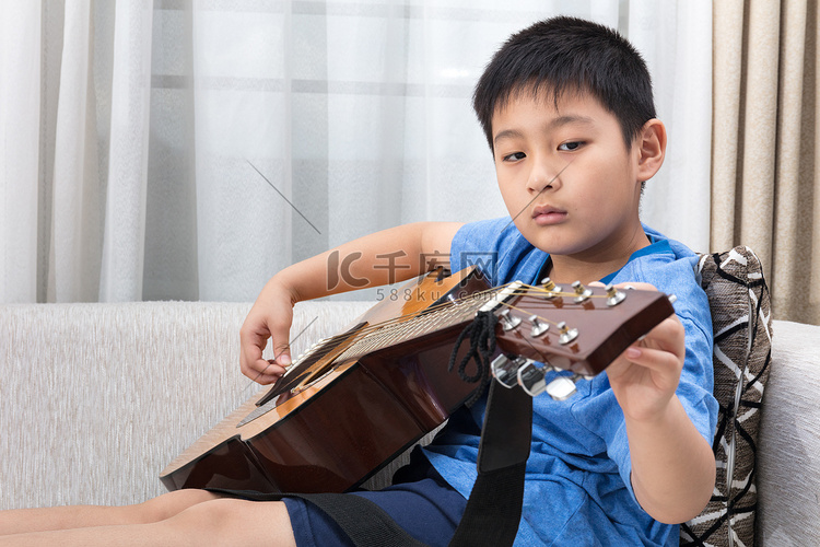 亚洲的中国小男孩坐在沙发上弹吉