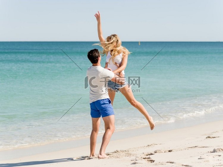 快乐的情侣在海滩度假中跳跃。年