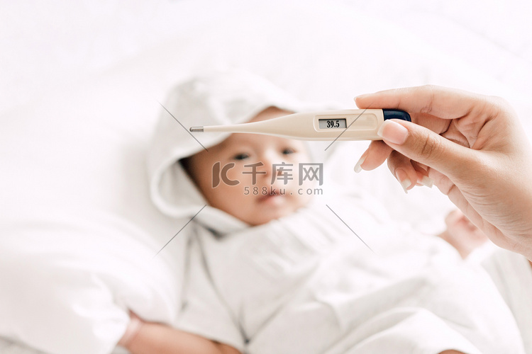 母亲拿着她生病婴儿的体温计。床