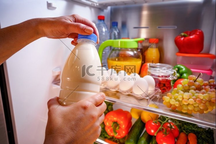 一位女士从打开的冰箱里取出牛奶
