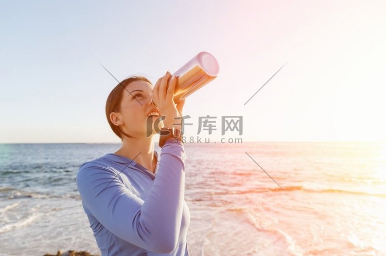 一名妇女在海滩上喝水。年轻女子