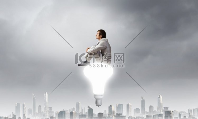一位年轻的商人坐在灯泡顶上思考