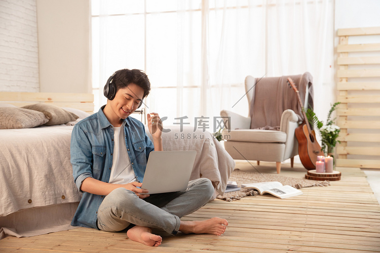 年轻的男青年坐在地板上使用笔记