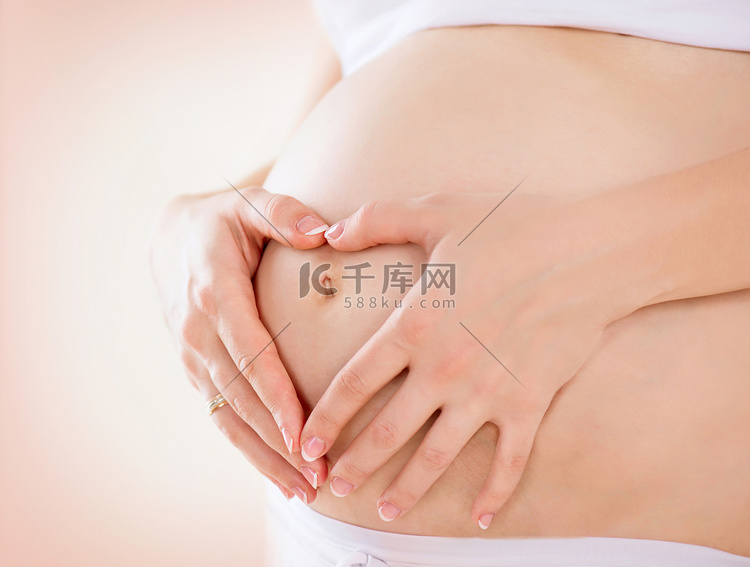 怀孕的妇女在她的肚皮上的心形手