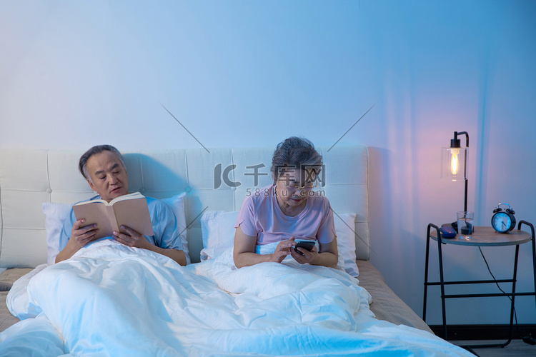 老年夫妇坐在床上用平板电脑看视