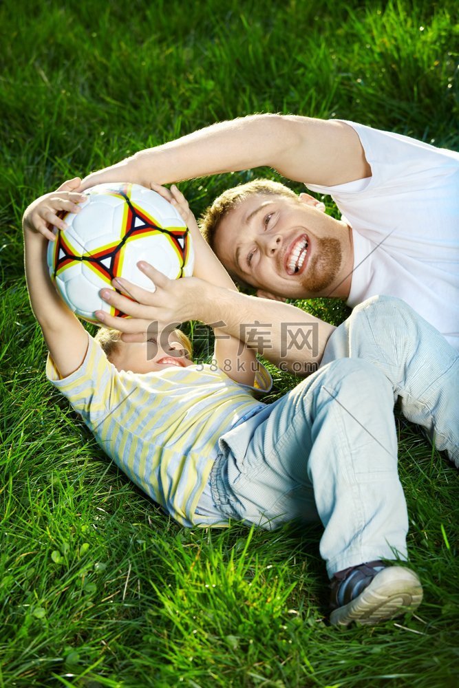 爸爸和儿子在草坪上为球而挣扎
