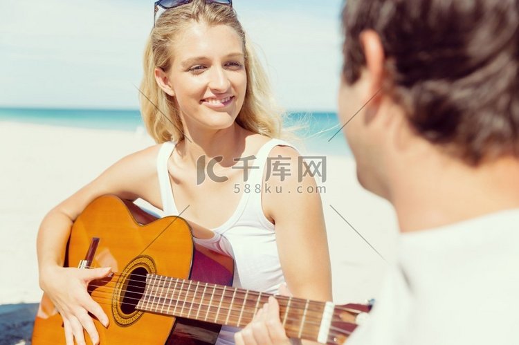 美丽的年轻女子在海滩上弹吉他。