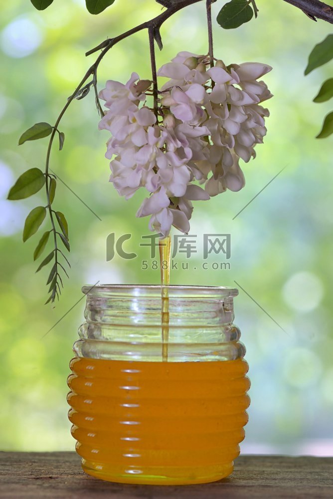 桌上放着一罐倒入蜂蜜的金合欢花