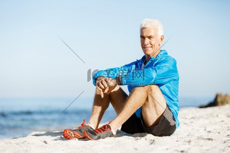 穿着运动服的男人坐在海滩上。穿