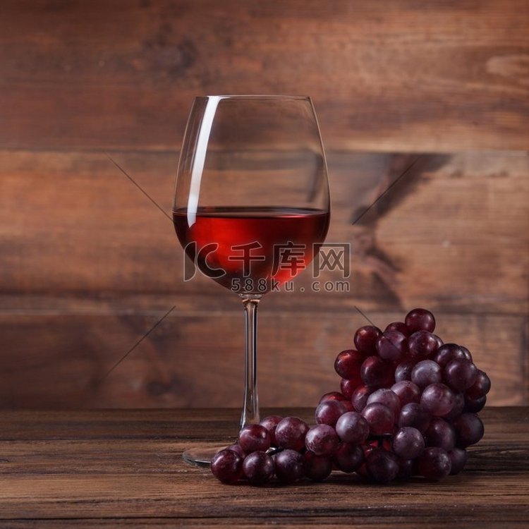 玻璃杯中的红酒，木头上有葡萄。