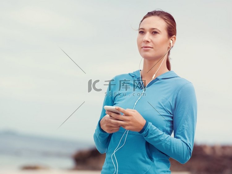 戴着耳机的运动年轻女子在海边