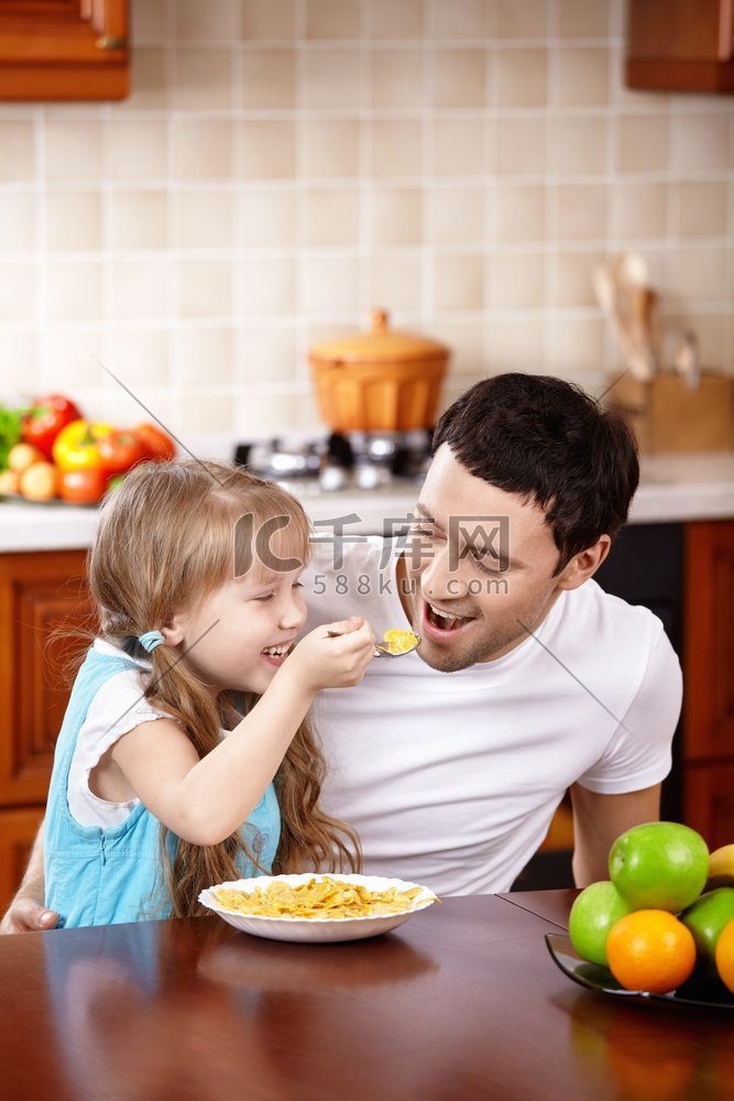 小女孩在厨房里用勺子喂爸爸