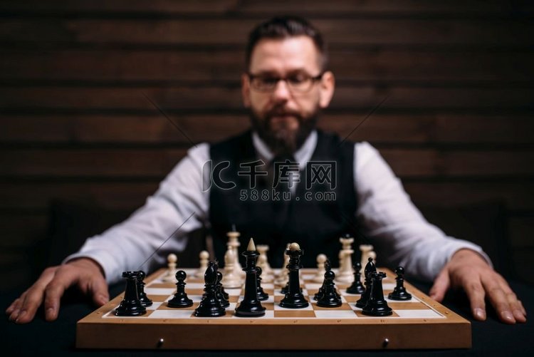 戴眼镜的男玩家坐在棋盘上，棋子