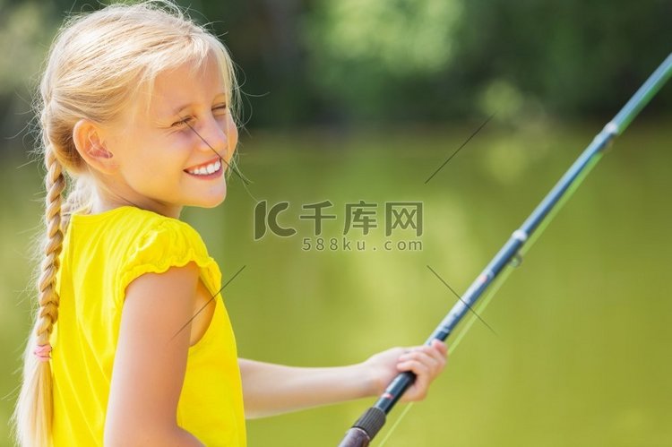 可爱的女孩坐在岸边钓鱼的肖像