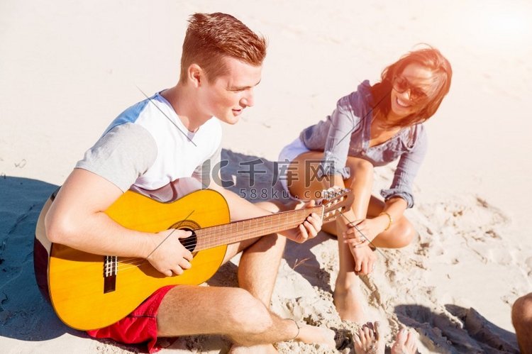 美丽的年轻人在海滩上弹着吉他。