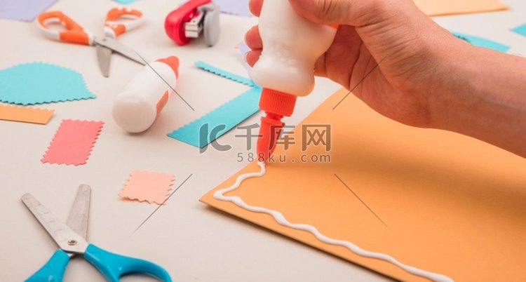 人手用剪刀在橙色纸上涂抹白色胶