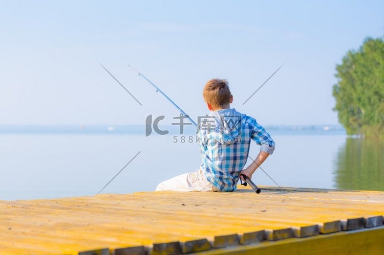 男孩在蓝色衬衫坐在码头与钓竿由