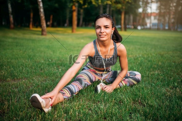 女孩在运动服和耳机坐在草地在夏