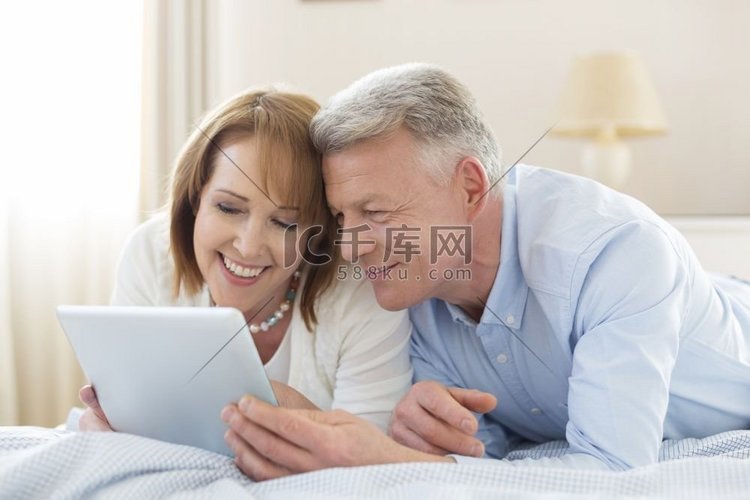 微笑的成熟夫妇在家躺在床上分享