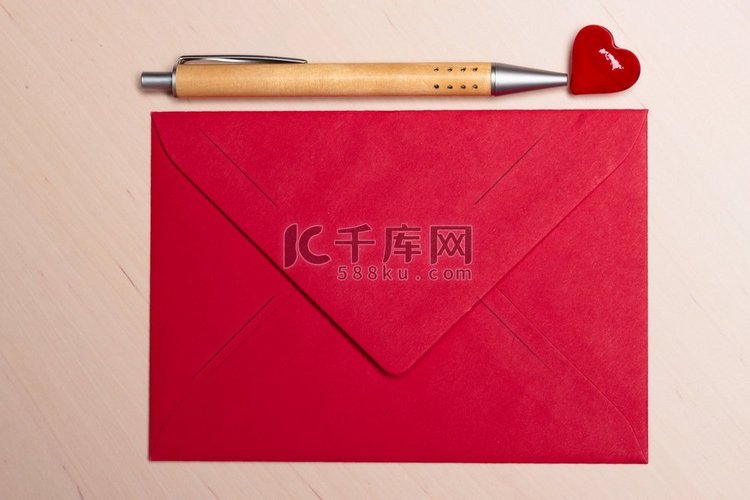 红色空白信封小心和笔在木表面。