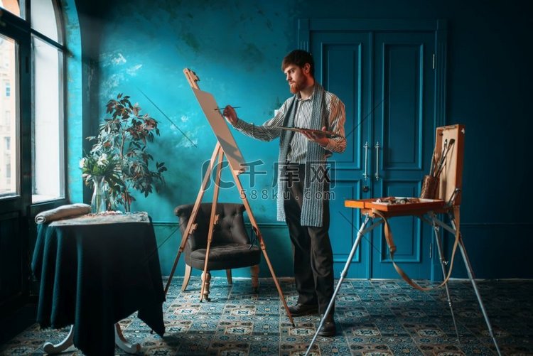 男性艺术家，在窗前的画架上用调