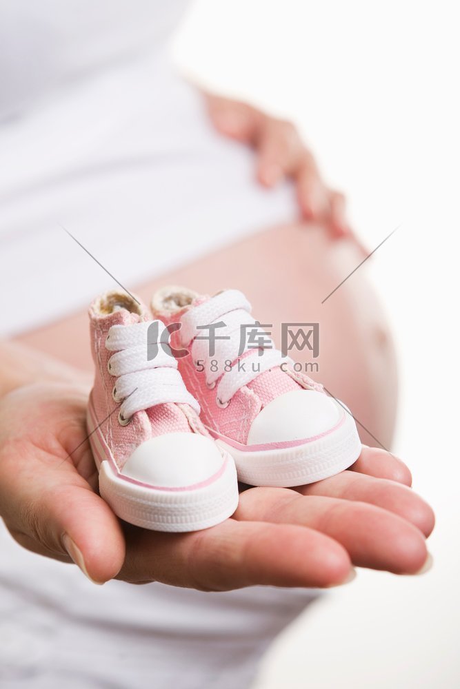 孕妇拿着一双粉红色的鞋子为女婴