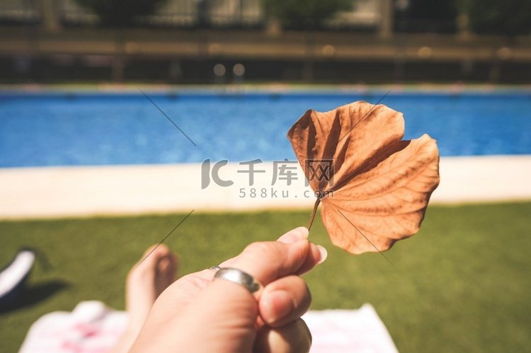 手持一片干枯的叶子靠近游泳池