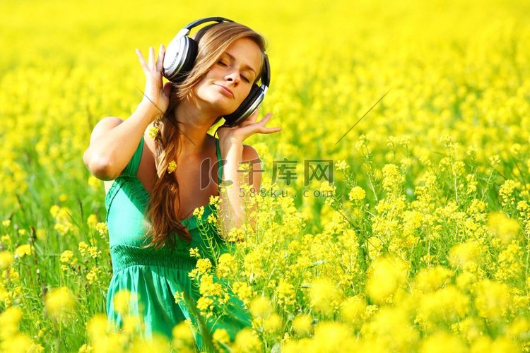 有耳机的年轻妇女听音乐在油籽花