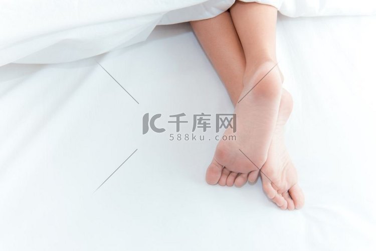 女人的脚在白色毯子下的床上。睡