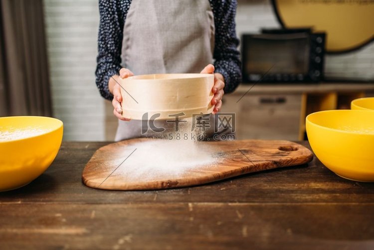 女人用木桌上的筛子过滤面粉。做