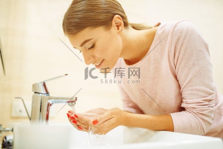 年轻妇女在洗手间的水槽洗她的脸