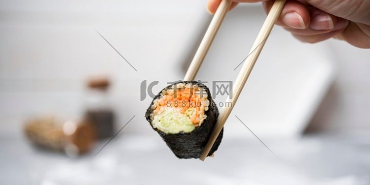 特写寿司卷与蔬菜举行筷子