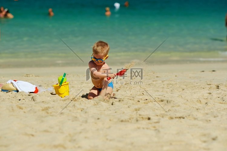 蹒跚学步的男孩在沙滩上玩铲子和