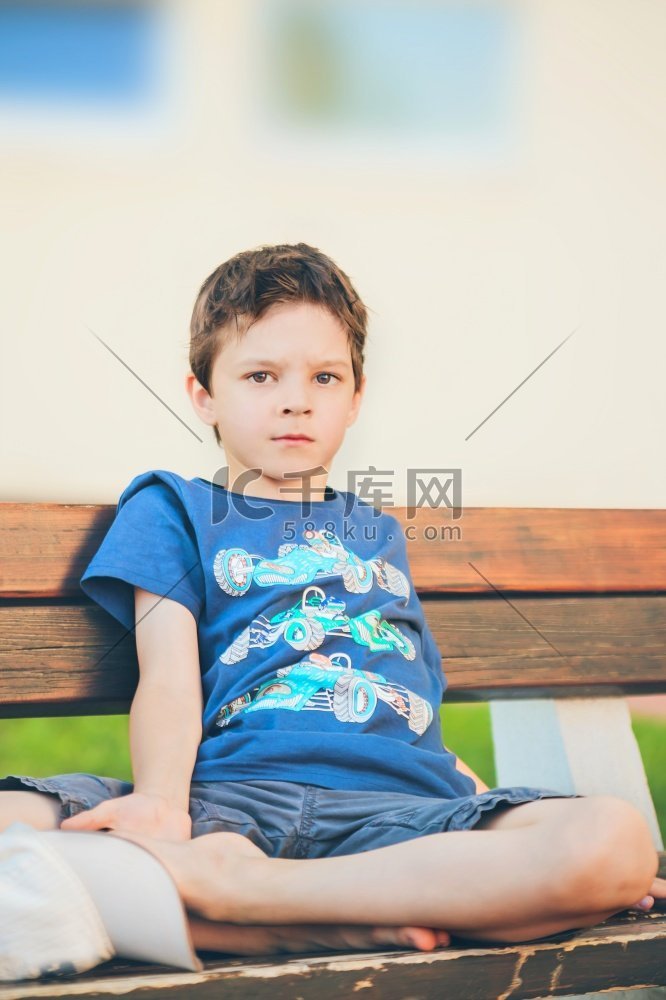 一个可怜的男孩坐在长凳上看着摄