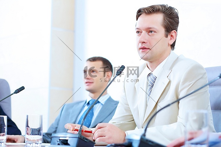 两位商人坐在会议桌旁用麦克风讲