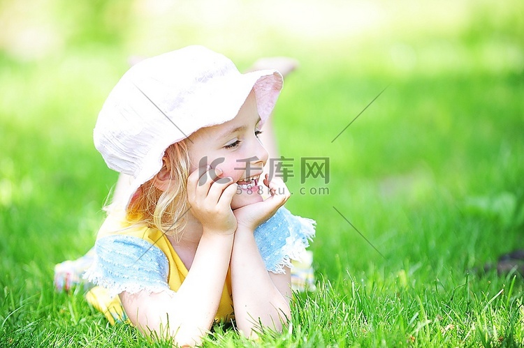帽子的顽皮的小女孩在草地上。五