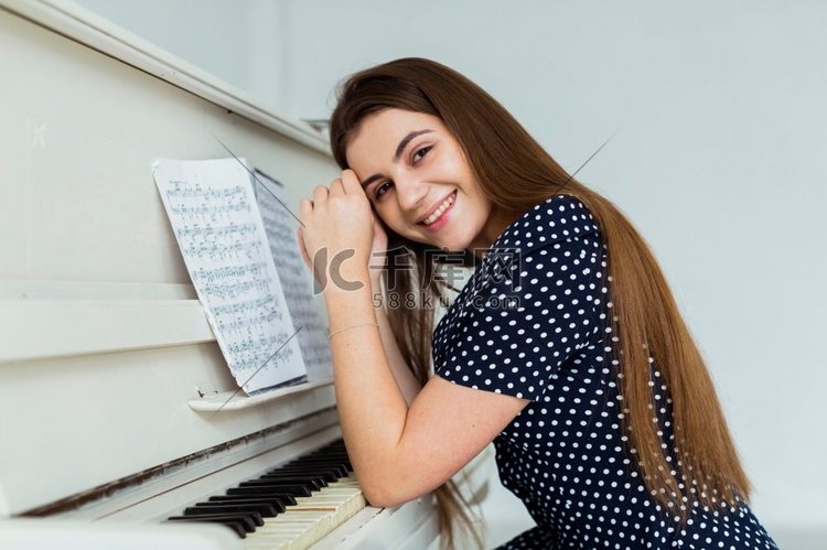 肖像微笑着的年轻女子靠在钢琴上