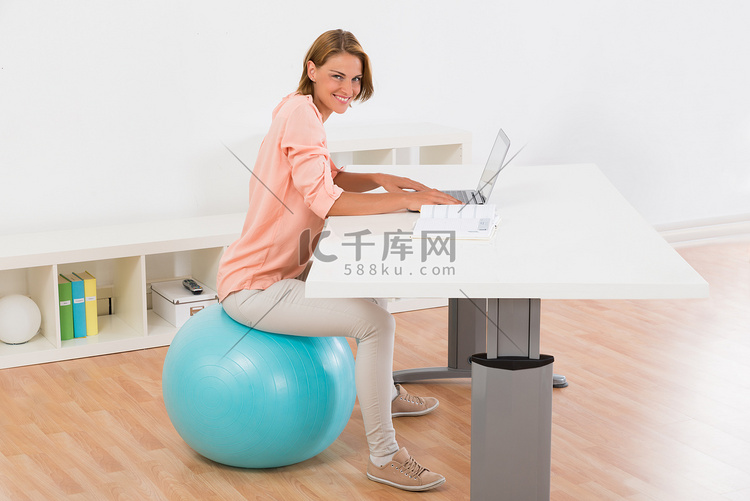 女人坐在健身球使用笔记本电脑