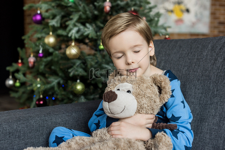 可爱的小孩穿着睡衣拥抱泰迪熊睡
