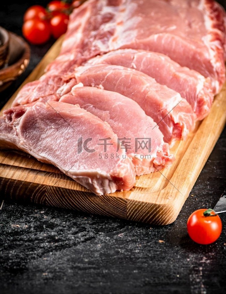 生猪肉切片在木砧板上。黑色背景