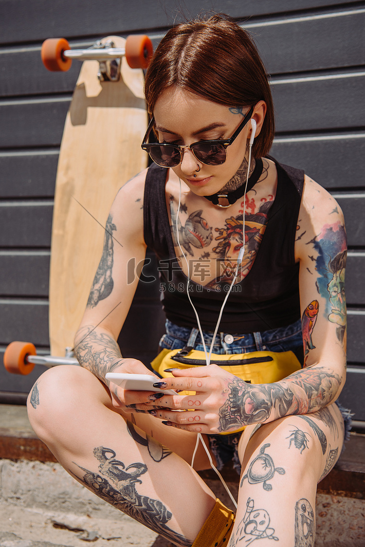 年轻纹身妇女在耳机听音乐与智能