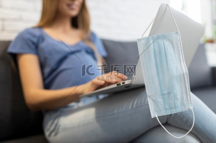 带医用口罩的孕妇坐在沙发上工作