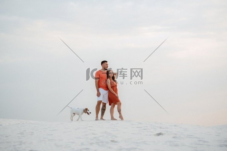 年轻夫妇橙色衣服与狗在沙漠白色